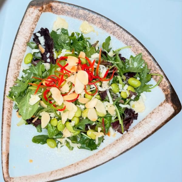A triangular plate of Delhi to Kathmandu salad with greens, edamame, almonds, and red peppers.
