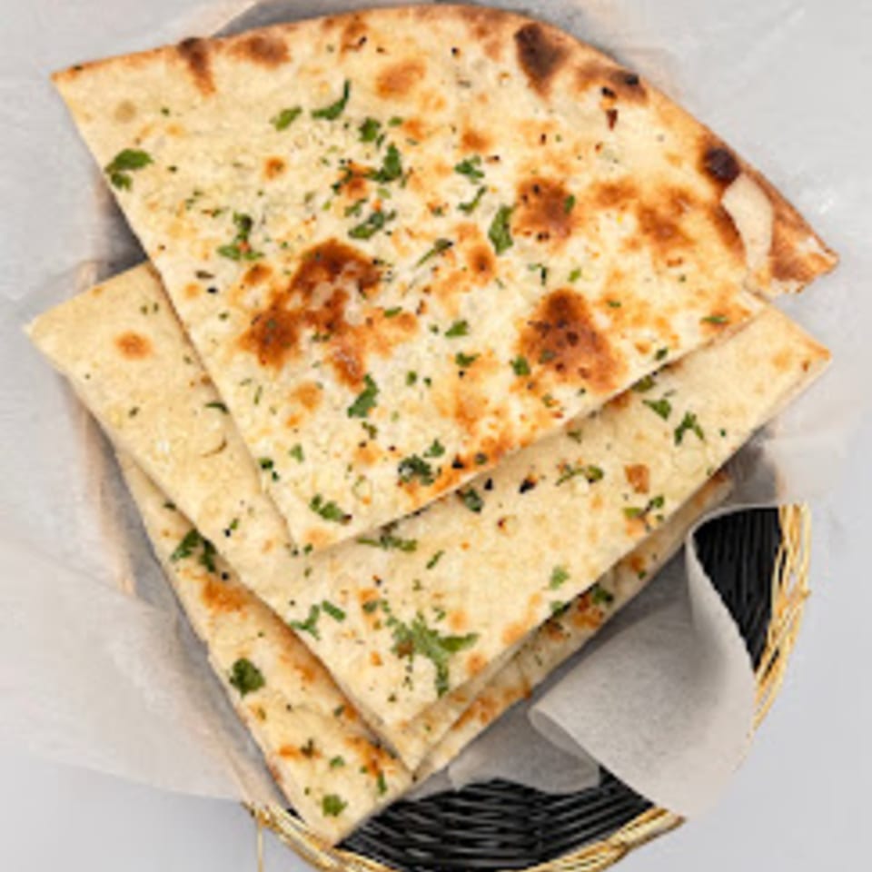 Golden brown Indian naan bread, garnished with green herbs, served in a basket lined with white paper.