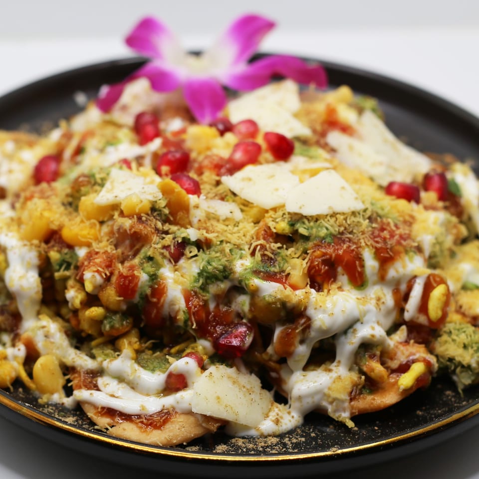 Indian chaat with yogurt, chutneys, pomegranate seeds, and spices, garnished with an orchid.