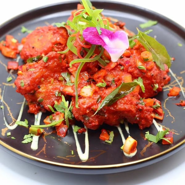 Delhi to Kathmandu's vibrant red Indian dish, garnished with fresh herbs and a pink flower.
