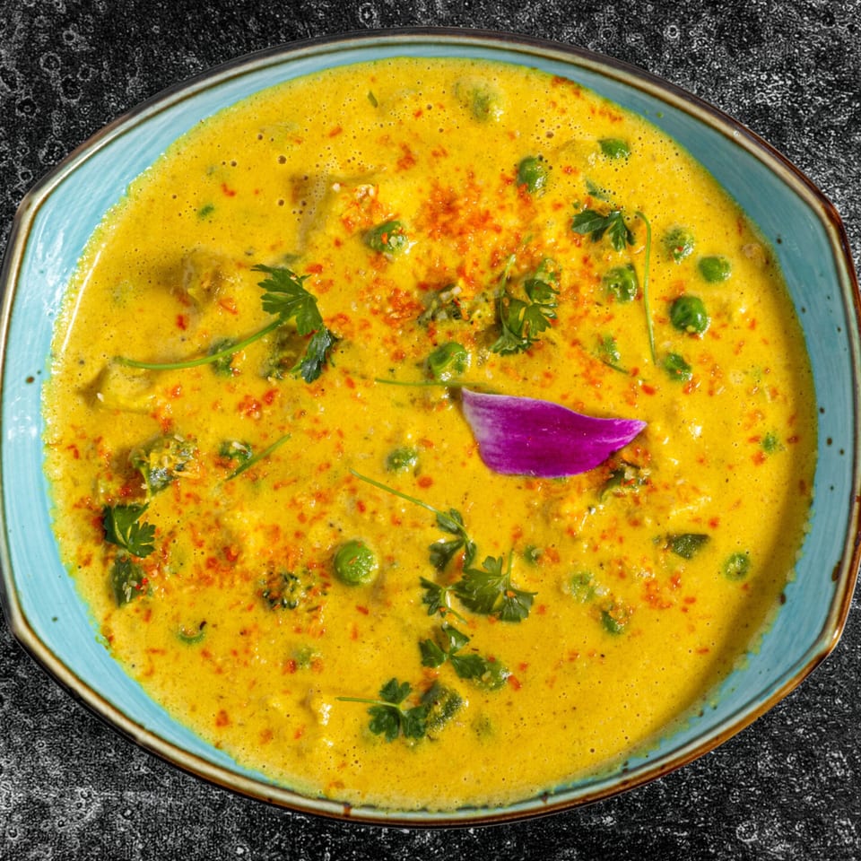 Indian curry with peas, cilantro, and a purple flower petal in a blue bowl.