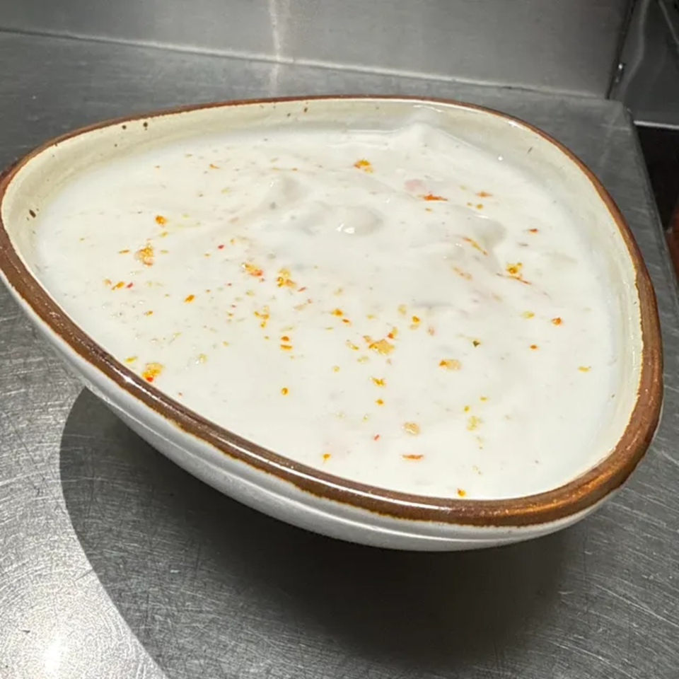 A bowl of Indian raita, a white yogurt-based sauce with orange spices, on a metal surface.