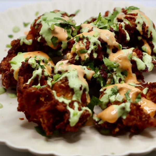 Crispy Indian pakoras drizzled with green and orange sauces, garnished with fresh cilantro.