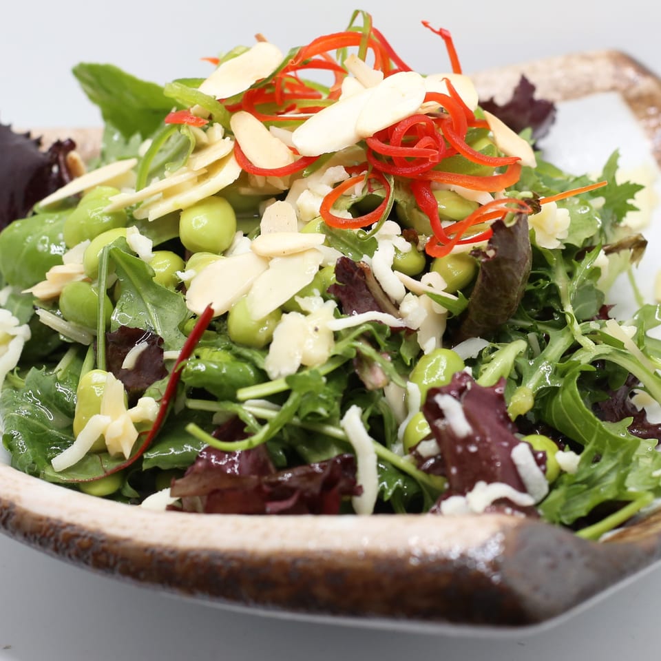 A vibrant Indian salad with mixed greens, edamame, sliced almonds, and red chili strips in a decorative bowl.
