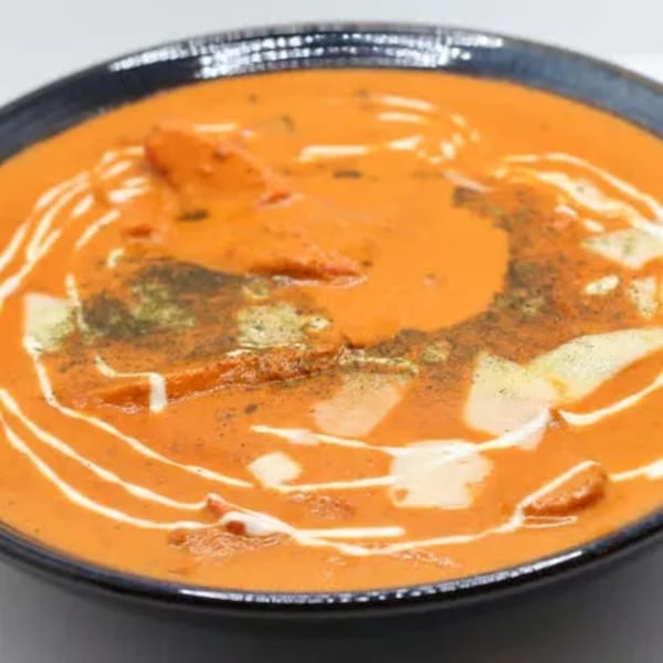 A close-up of Indian butter chicken, garnished with cream swirls and herbs in a black bowl.