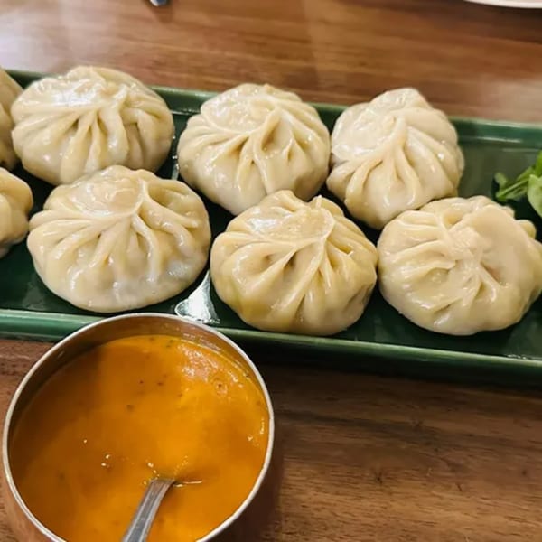 A green plate of steamed momos with a side of orange dipping sauce from Delhi to Kathmandu.