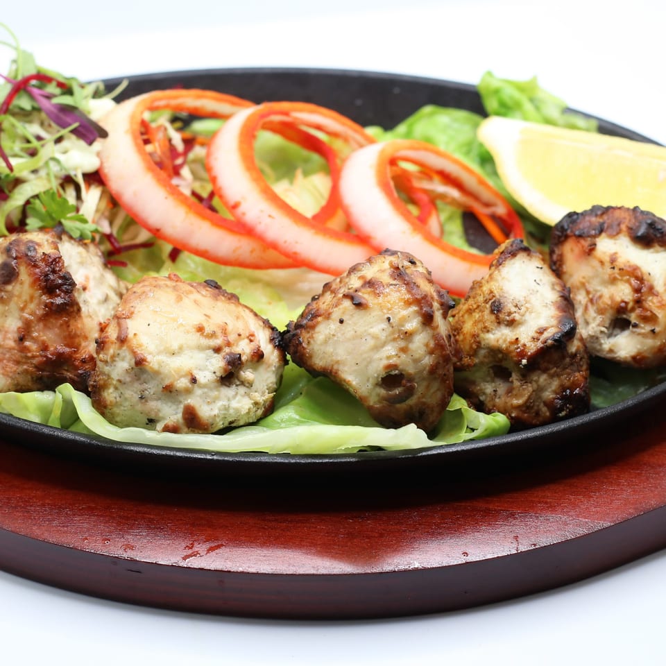 Indian chicken tikka with salad, onion rings, and a lemon wedge on a sizzling platter.
