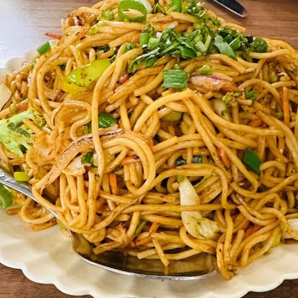 A large serving of Indian noodles with vegetables and green onions on a white plate.