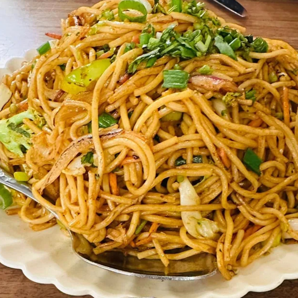 A large serving of Indian noodles with vegetables and green onions on a white plate.