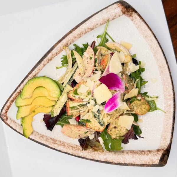 A triangular plate of Indian salad with greens, avocado, cheese, and a purple orchid garnish.
